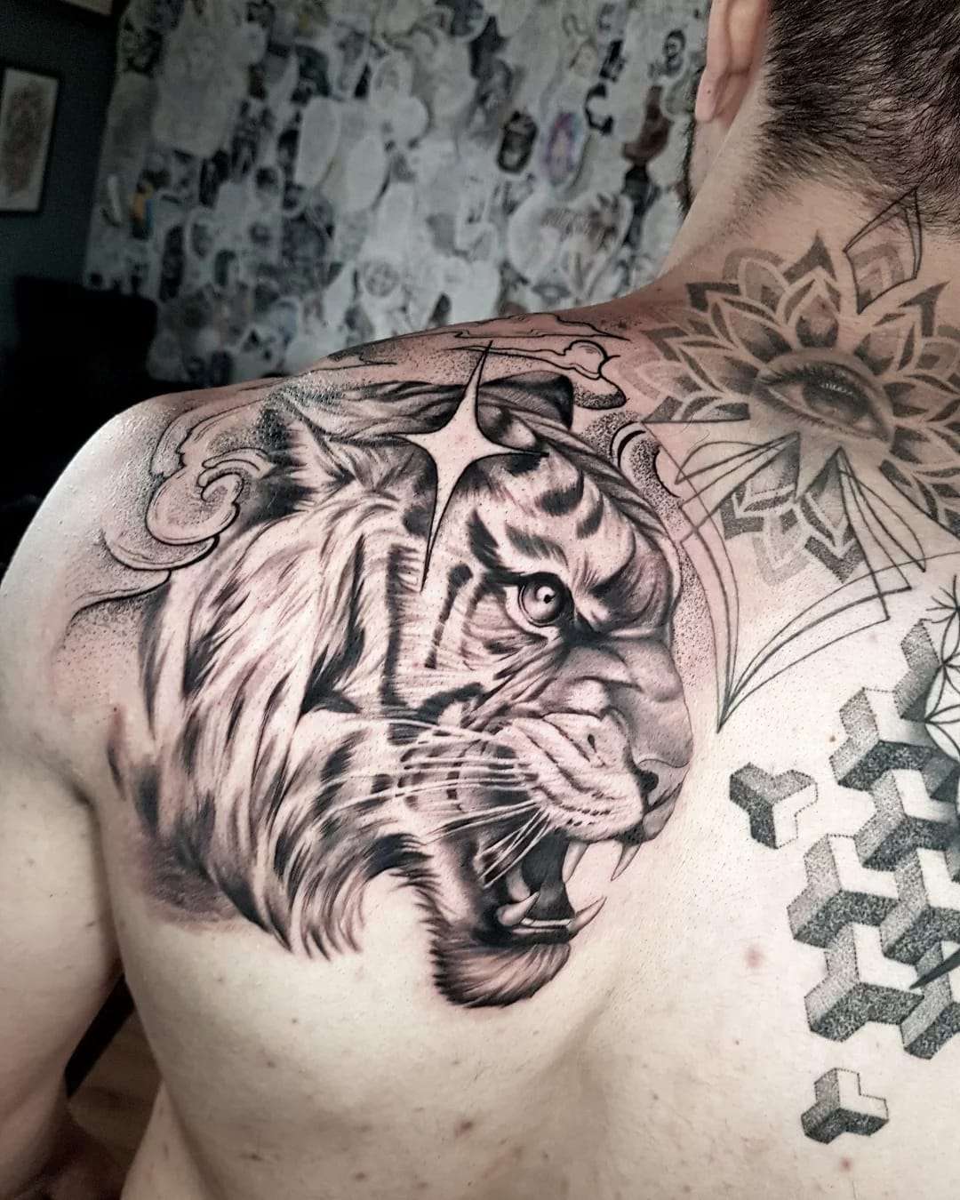 Tatuagem realista de um tigre rugindo, em preto e cinza, cobrindo o ombro e o peito